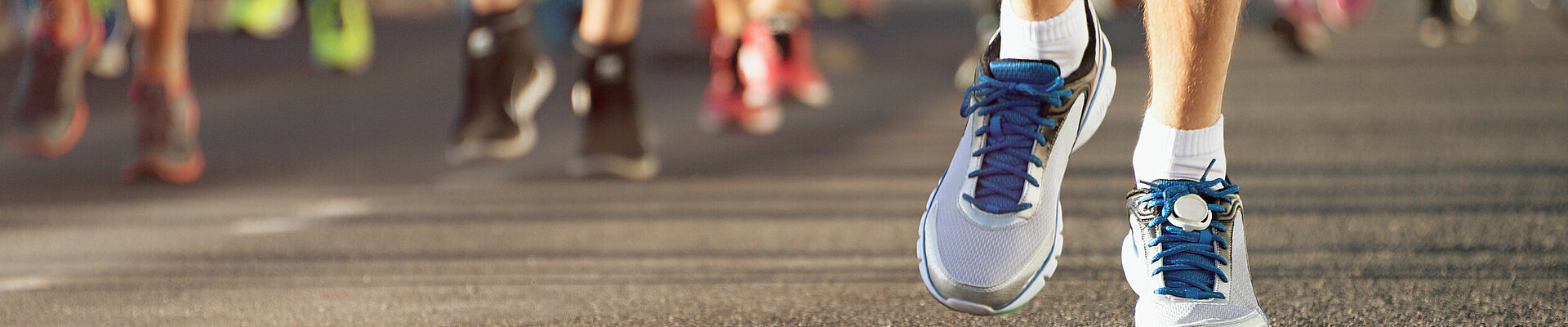 Nahaufnahme der Sportschuhe mehrerer Läufer während eines Marathons, die sich auf der Strecke fortbewegen.