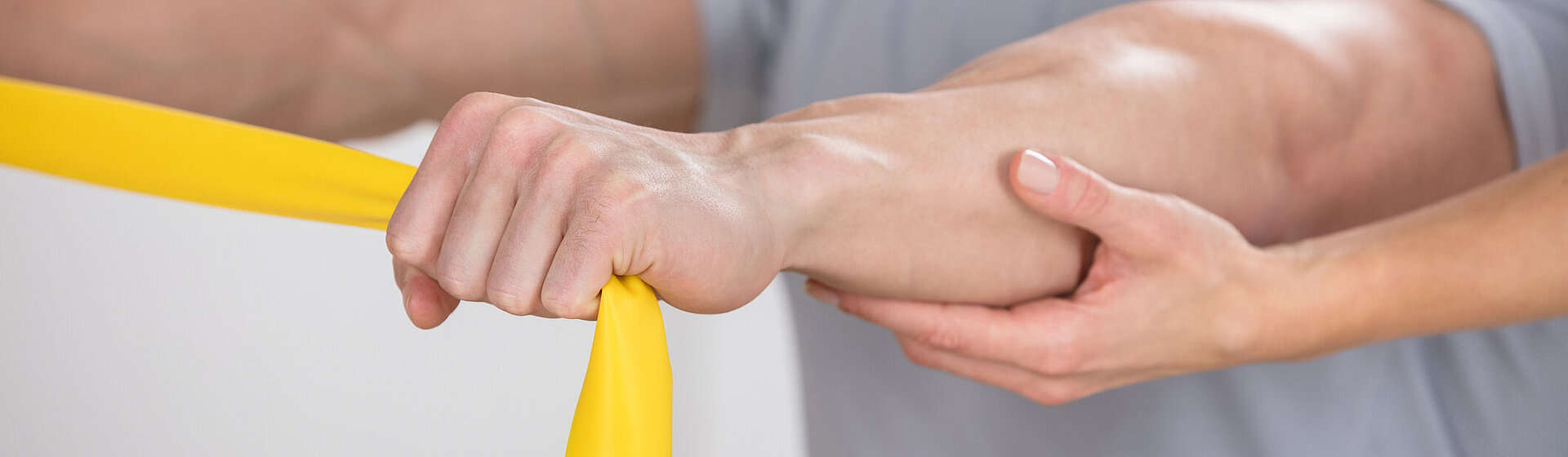Eine männliche Person hält ein Band in seinen nach vorne gestreckten Händen, hinter ihm eine Person die mit einer Hand die richtige Haltung unterstützt